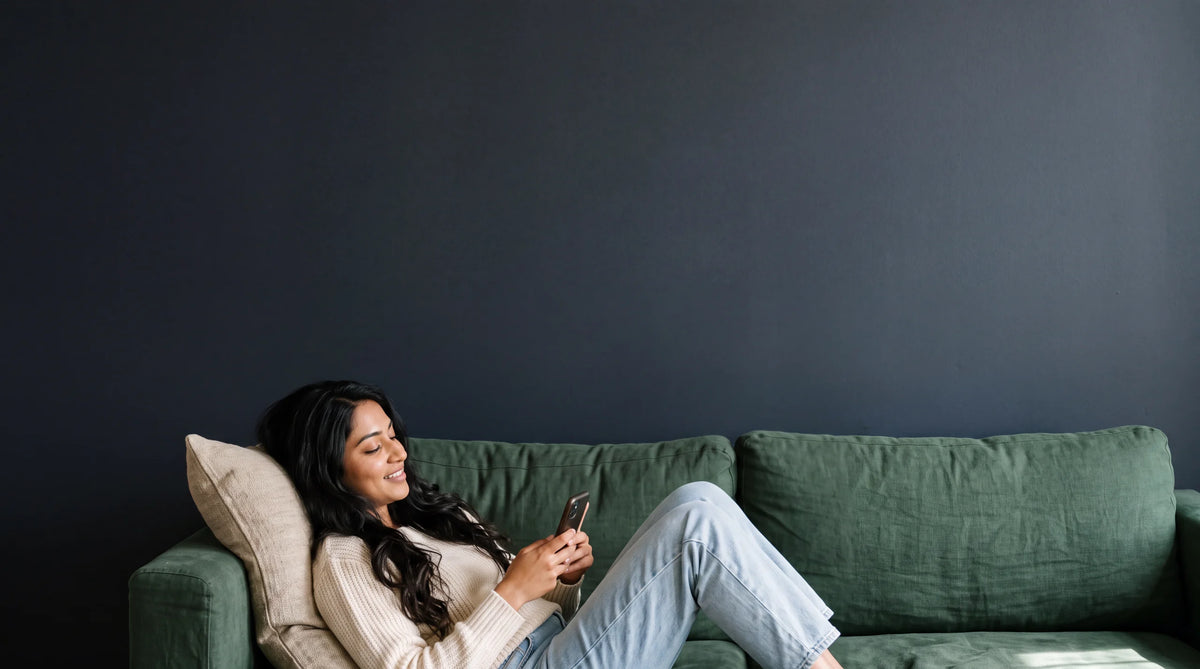 A woman relaxing on a green sofa in the evening, looking at her phone
